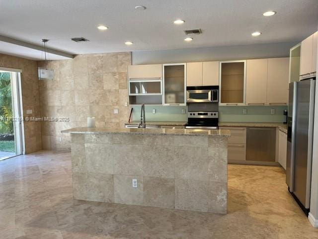 kitchen with appliances with stainless steel finishes, sink, a kitchen island with sink, and light stone countertops