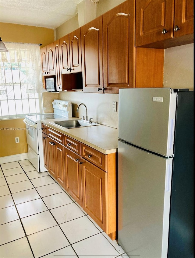 kitchen featuring sink, a textured ceiling, light tile patterned floors, stainless steel fridge, and white range with electric cooktop