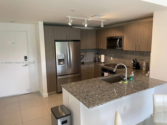 kitchen featuring sink, tasteful backsplash, kitchen peninsula, dark stone counters, and appliances with stainless steel finishes