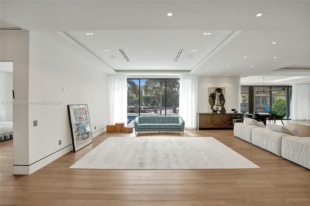 unfurnished living room with an inviting chandelier, a tray ceiling, and light hardwood / wood-style flooring