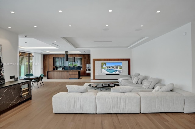 living room featuring a raised ceiling, light wood-type flooring, and an inviting chandelier