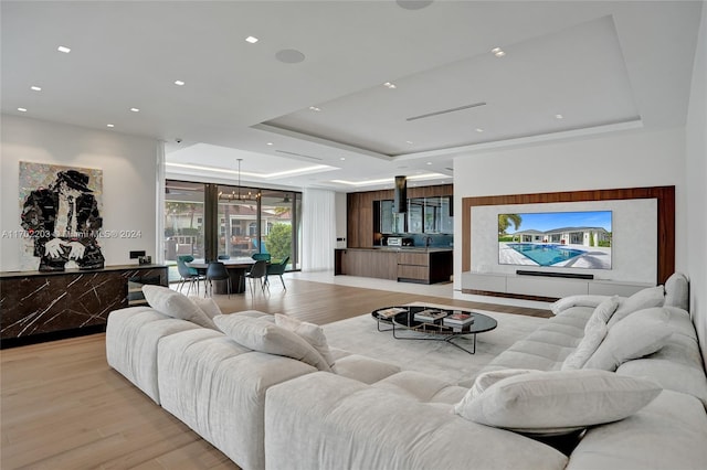 living room featuring a tray ceiling, sink, light hardwood / wood-style floors, and an inviting chandelier