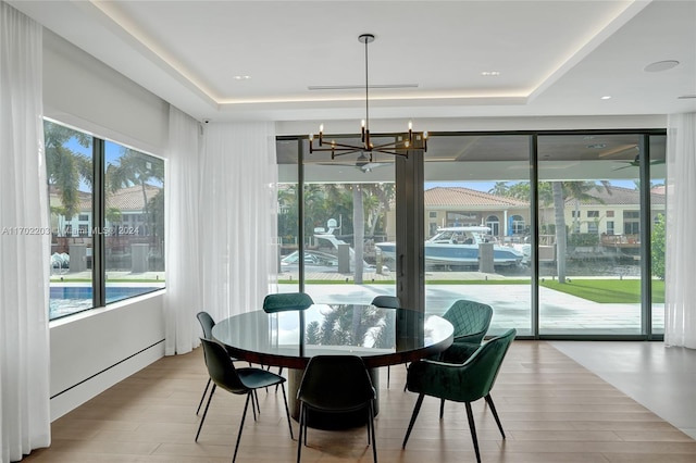 dining space with a notable chandelier, a raised ceiling, and light hardwood / wood-style flooring