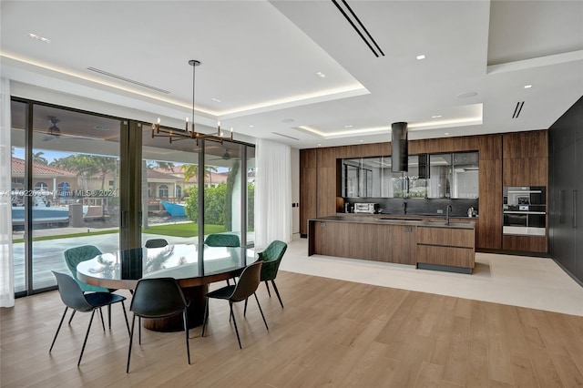 dining space featuring an inviting chandelier, a tray ceiling, light hardwood / wood-style flooring, and sink