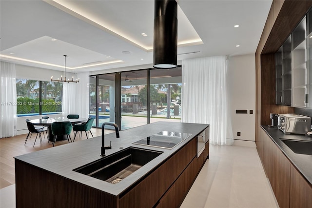 kitchen with black electric stovetop, a tray ceiling, a spacious island, sink, and a chandelier