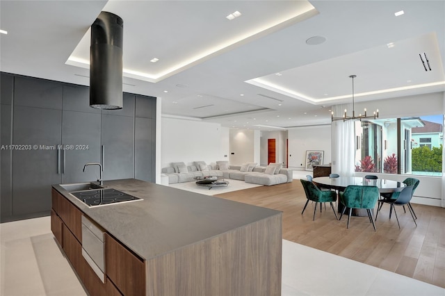 kitchen with a tray ceiling, a large island, hanging light fixtures, and light wood-type flooring