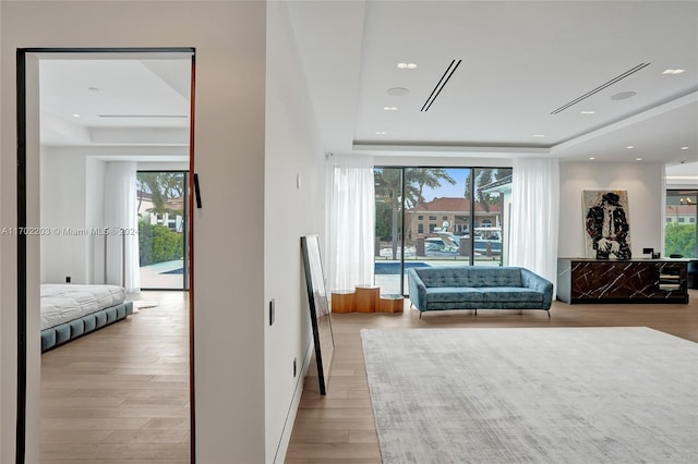 bedroom featuring light wood-type flooring, a raised ceiling, and multiple windows