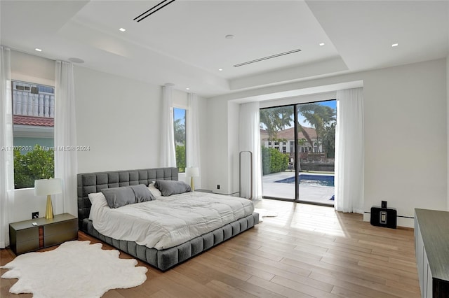 bedroom featuring a tray ceiling, access to outside, and light hardwood / wood-style flooring