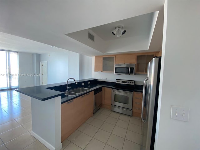 kitchen featuring sink, light tile patterned floors, appliances with stainless steel finishes, a tray ceiling, and kitchen peninsula