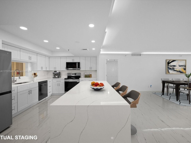 kitchen with appliances with stainless steel finishes, a kitchen breakfast bar, marble finish floor, white cabinetry, and a sink