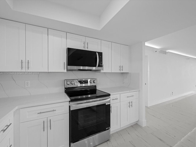 kitchen featuring white cabinets, decorative backsplash, stainless steel appliances, and light stone counters