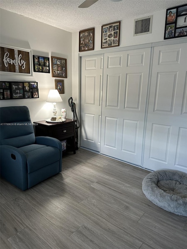 living area featuring ceiling fan, wood-type flooring, and a textured ceiling