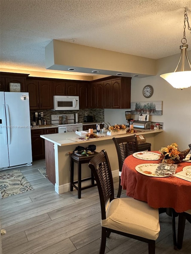 kitchen with decorative light fixtures, light wood-type flooring, white appliances, and dark brown cabinetry