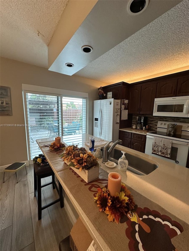 kitchen with tasteful backsplash, white appliances, dark brown cabinetry, sink, and light hardwood / wood-style floors