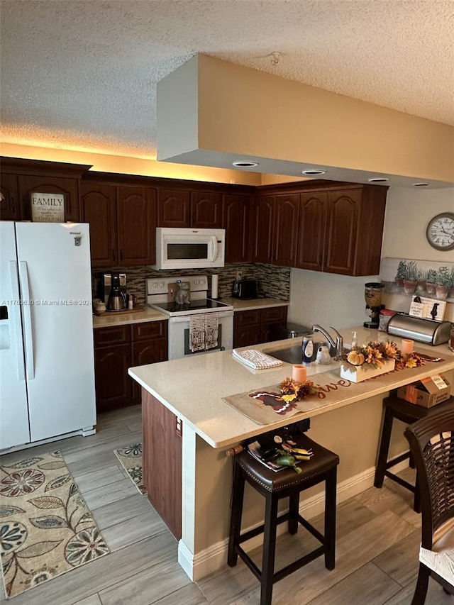 kitchen with dark brown cabinetry, sink, light hardwood / wood-style flooring, white appliances, and a kitchen bar