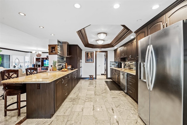 kitchen with stainless steel appliances, a tray ceiling, a breakfast bar, and dark brown cabinets