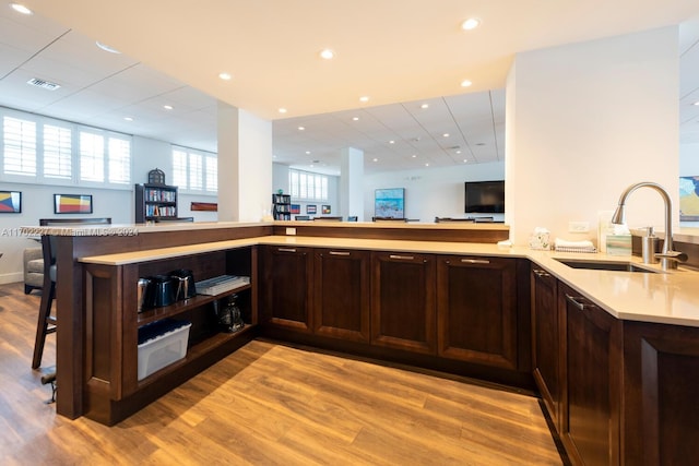 kitchen with kitchen peninsula, a kitchen bar, dark brown cabinetry, sink, and light hardwood / wood-style floors