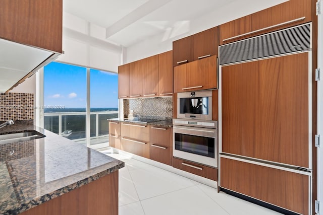 kitchen featuring backsplash, paneled built in fridge, a water view, sink, and light tile patterned floors