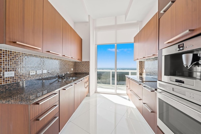 kitchen featuring decorative backsplash, stainless steel double oven, sink, light tile patterned floors, and dark stone countertops