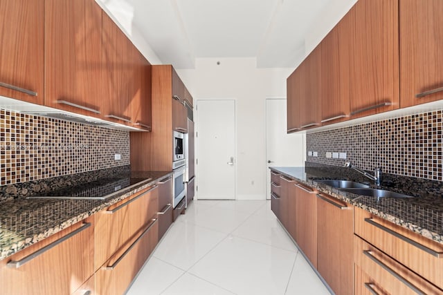 kitchen featuring light tile patterned floors, backsplash, dark stone counters, and sink