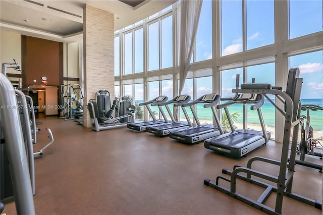 exercise room with a towering ceiling, a water view, and a beach view