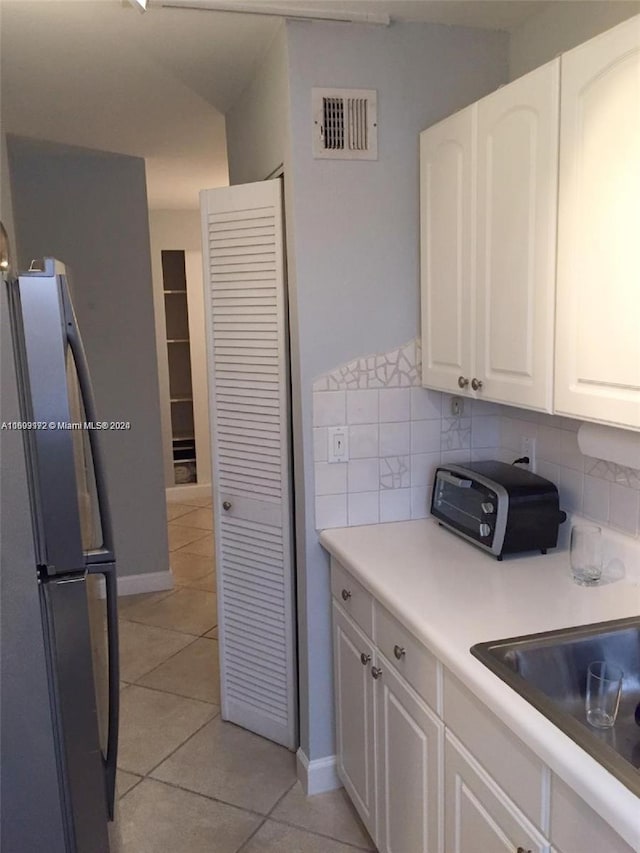 kitchen with light tile patterned floors, backsplash, white cabinetry, and stainless steel refrigerator