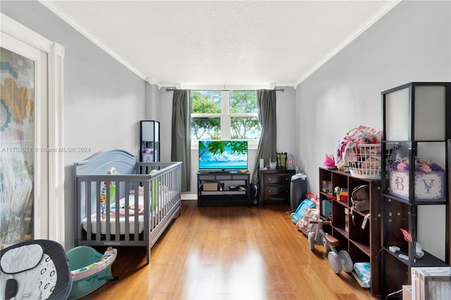 bedroom featuring a textured ceiling, crown molding, light hardwood / wood-style flooring, and a nursery area