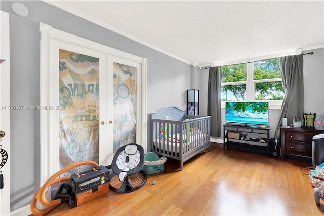 bedroom featuring french doors, wood-type flooring, ornamental molding, a textured ceiling, and a crib