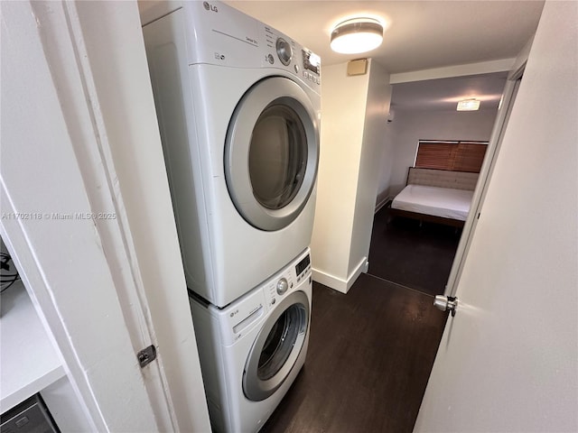 laundry area with baseboards, stacked washer and clothes dryer, dark wood finished floors, and laundry area