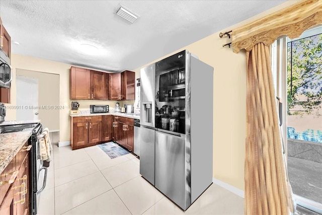 kitchen with a textured ceiling, light stone counters, light tile patterned floors, and stainless steel appliances