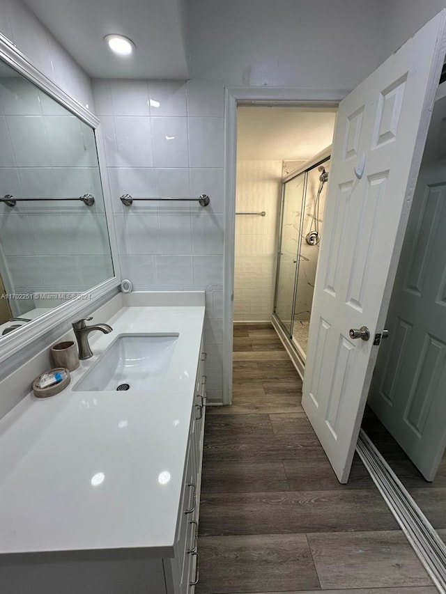 bathroom with hardwood / wood-style floors, vanity, walk in shower, and tile walls