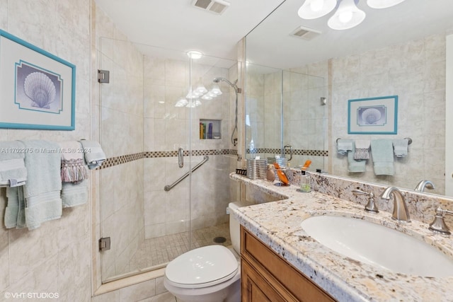 bathroom with a shower with door, vanity, tile walls, and toilet