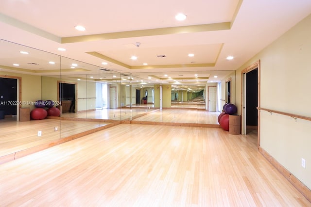 workout area with a raised ceiling and light hardwood / wood-style flooring