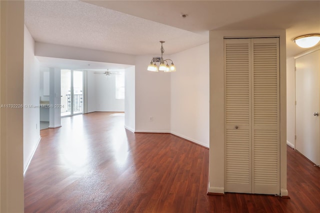 empty room featuring ceiling fan with notable chandelier, a textured ceiling, and dark hardwood / wood-style flooring