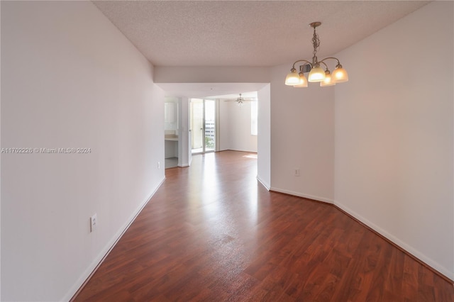 empty room featuring ceiling fan with notable chandelier, a textured ceiling, and dark wood-type flooring