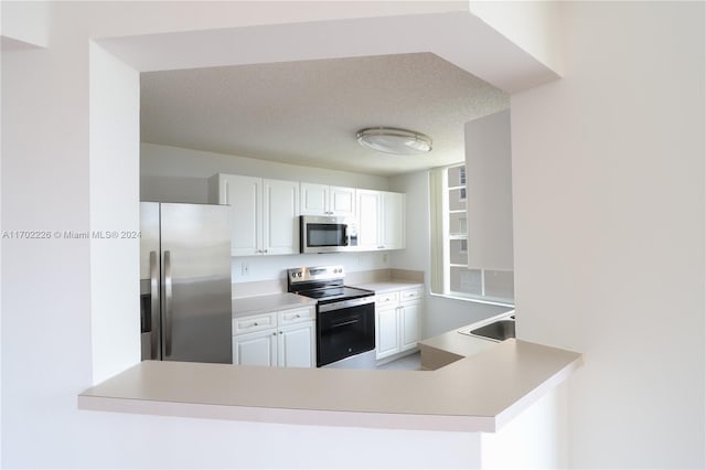 kitchen with kitchen peninsula, appliances with stainless steel finishes, a textured ceiling, sink, and white cabinetry