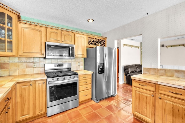 kitchen with tasteful backsplash, a textured ceiling, stainless steel appliances, light tile patterned floors, and tile counters