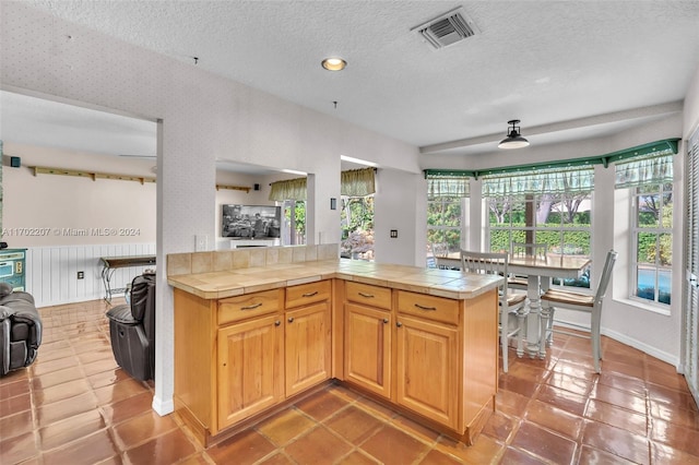 kitchen featuring tile countertops, kitchen peninsula, a textured ceiling, and tile patterned flooring