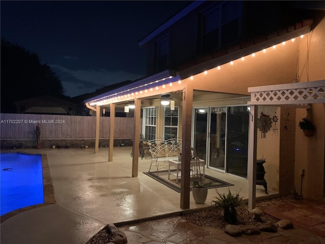 patio at night featuring a fenced in pool