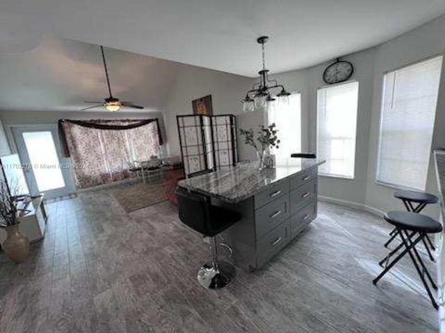 kitchen featuring lofted ceiling, dark wood-type flooring, ceiling fan with notable chandelier, gray cabinets, and light stone countertops