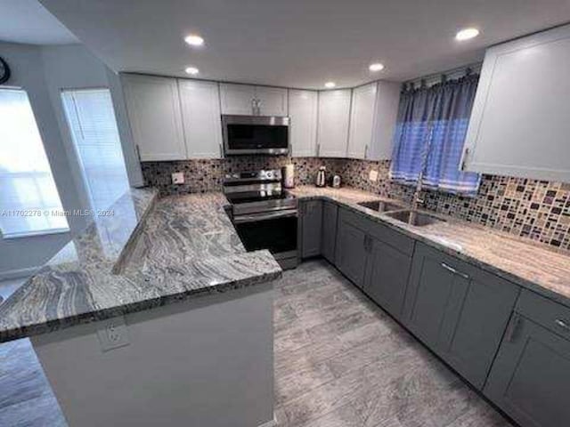 kitchen with kitchen peninsula, appliances with stainless steel finishes, light stone counters, and sink