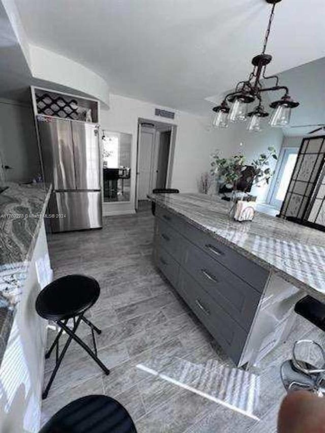 kitchen featuring light stone countertops, stainless steel fridge, pendant lighting, an inviting chandelier, and gray cabinets