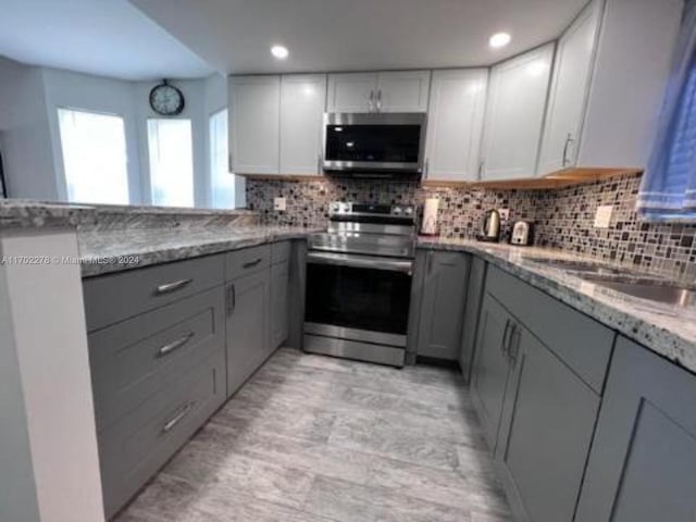 kitchen featuring gray cabinetry, light wood-type flooring, light stone countertops, appliances with stainless steel finishes, and tasteful backsplash