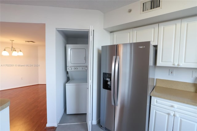 kitchen featuring hanging light fixtures, stainless steel refrigerator with ice dispenser, a chandelier, white cabinets, and stacked washer and clothes dryer