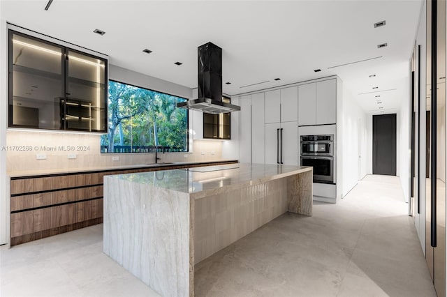 kitchen with white cabinetry, sink, tasteful backsplash, light stone counters, and a kitchen island