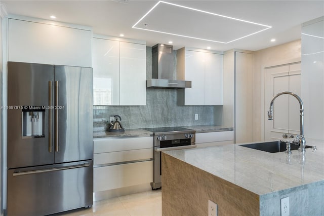 kitchen featuring light stone countertops, stainless steel appliances, a kitchen island with sink, wall chimney range hood, and white cabinetry