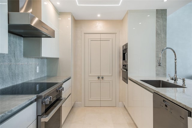 kitchen with wall chimney range hood, sink, light stone counters, white cabinetry, and stainless steel appliances