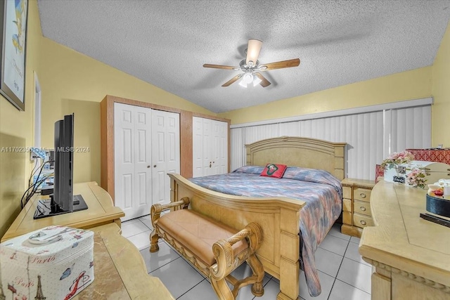 bedroom with a textured ceiling, vaulted ceiling, ceiling fan, multiple closets, and light tile patterned flooring