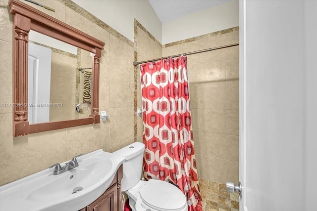 bathroom with curtained shower, a textured ceiling, toilet, vanity, and tile walls