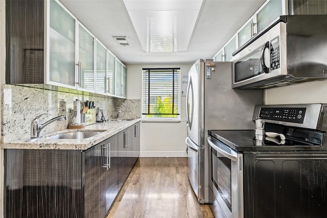 kitchen with backsplash, light stone counters, stainless steel appliances, sink, and wood-type flooring